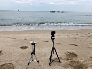 Image of a camera and a microphone set up to record at the seashore.